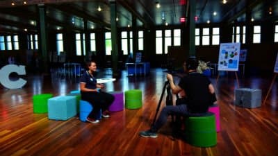 Holly from fizzics being interviewed by man with camera and woman on colourful stools in a hall