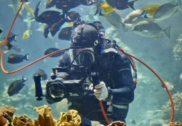 Scuba diver holding a camera pointing at reef outcrop