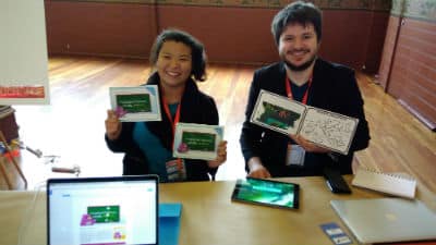 Aurora Reality man and woman holding books behind a desk with laptop and tablet