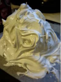 A mountain of white glossy meringue on a piece of white baking paper