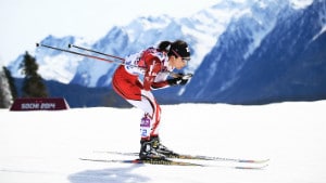 Cross country skiing athlete going down hill crouched mountains and snow in background