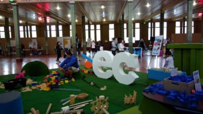 Indoor playground with green mat and kids playing with toys and parents looking on, big white letters ec people walking around 