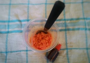 orange coloured bicarb soda with a spoon in a cup and some red food colouring next to it