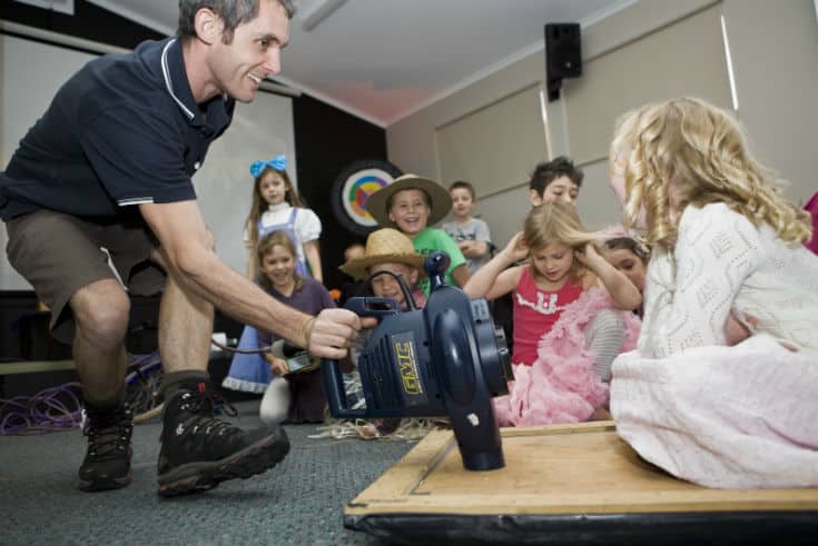 Leaf blower hovercraft; a Fizzics educator is moving a girl sitting on a wooden platform which has a running leaf blower attached