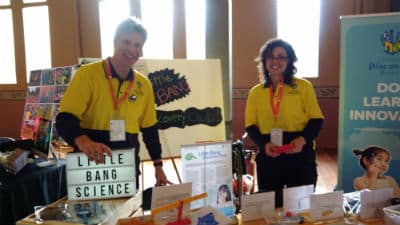 little bang science children's discovering museum Man and woman in yellow shirts standing behind table full of toys