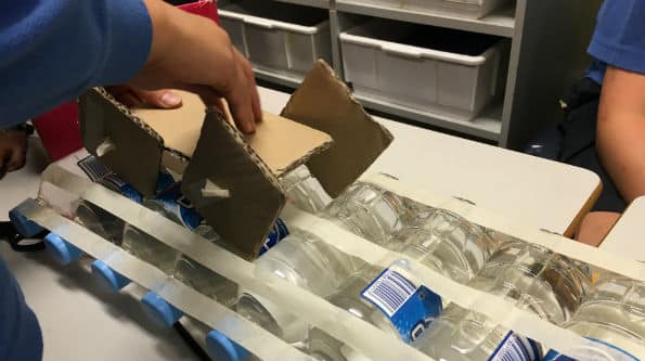 cardboard square wheel car going across a line of bottles