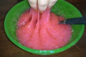 Hand grabbing glittery pink slime out of a green plastic bowl with a spoon in it