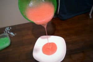 Pink slime being poured from a green bowl onto a white plate on a brown table