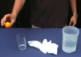Ping pong ball, glass, tissue paper and container of water on a black table