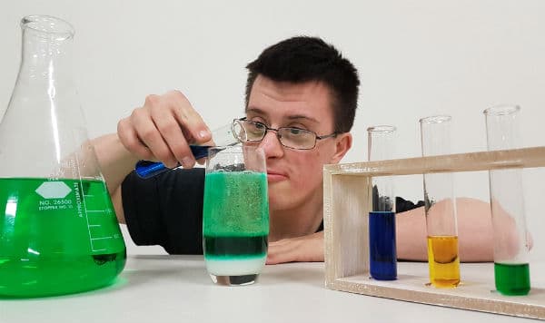 scienceability - student pouring blue liquid into a fizzing green test tube