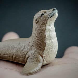 Person holding up a replica of a Sea lion in the palm of their hands. Front view